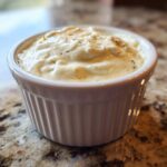 Close-up of creamy horseradish sauce for prime rib served in a small white fluted ramekin on a granite countertop.