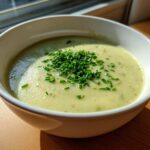 A close-up of a bowl of creamy, light green leek soup garnished generously with fresh chopped chives.