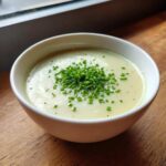 A creamy, pale yellow bowl of leek soup topped generously with fresh, chopped green chives.