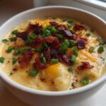 Close-up of a rich, creamy loaded baked potato soup topped with bacon bits and fresh green onions.