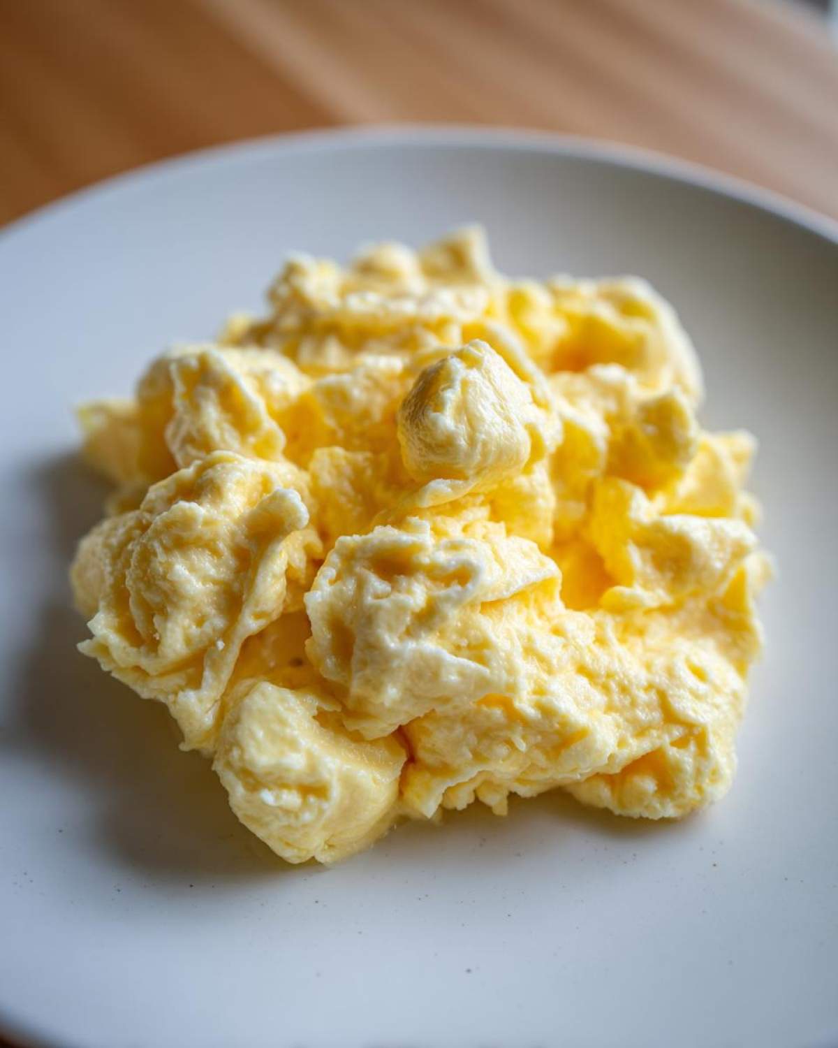 Close-up of perfectly creamy, soft scrambled eggs piled high on a light-colored plate.