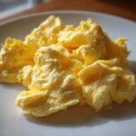 Close-up of fluffy, creamy scrambled eggs served on a white plate, highlighting their soft texture.