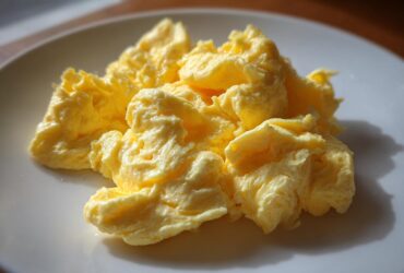 Close-up of fluffy, creamy scrambled eggs served on a white plate, highlighting their soft texture.
