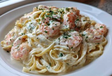 A close-up of creamy shrimp alfredo pasta, featuring pink shrimp tossed in rich white sauce and garnished with parsley.