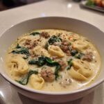 Close-up of a creamy tortellini soup featuring cheese tortellini, crumbled sausage, spinach, and grated Parmesan.
