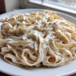 Close-up of fettuccine pasta coated in rich, creamy vegan alfredo sauce and topped with black pepper.