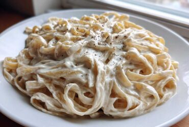 Close-up of fettuccine pasta coated in rich, creamy vegan alfredo sauce and topped with black pepper.