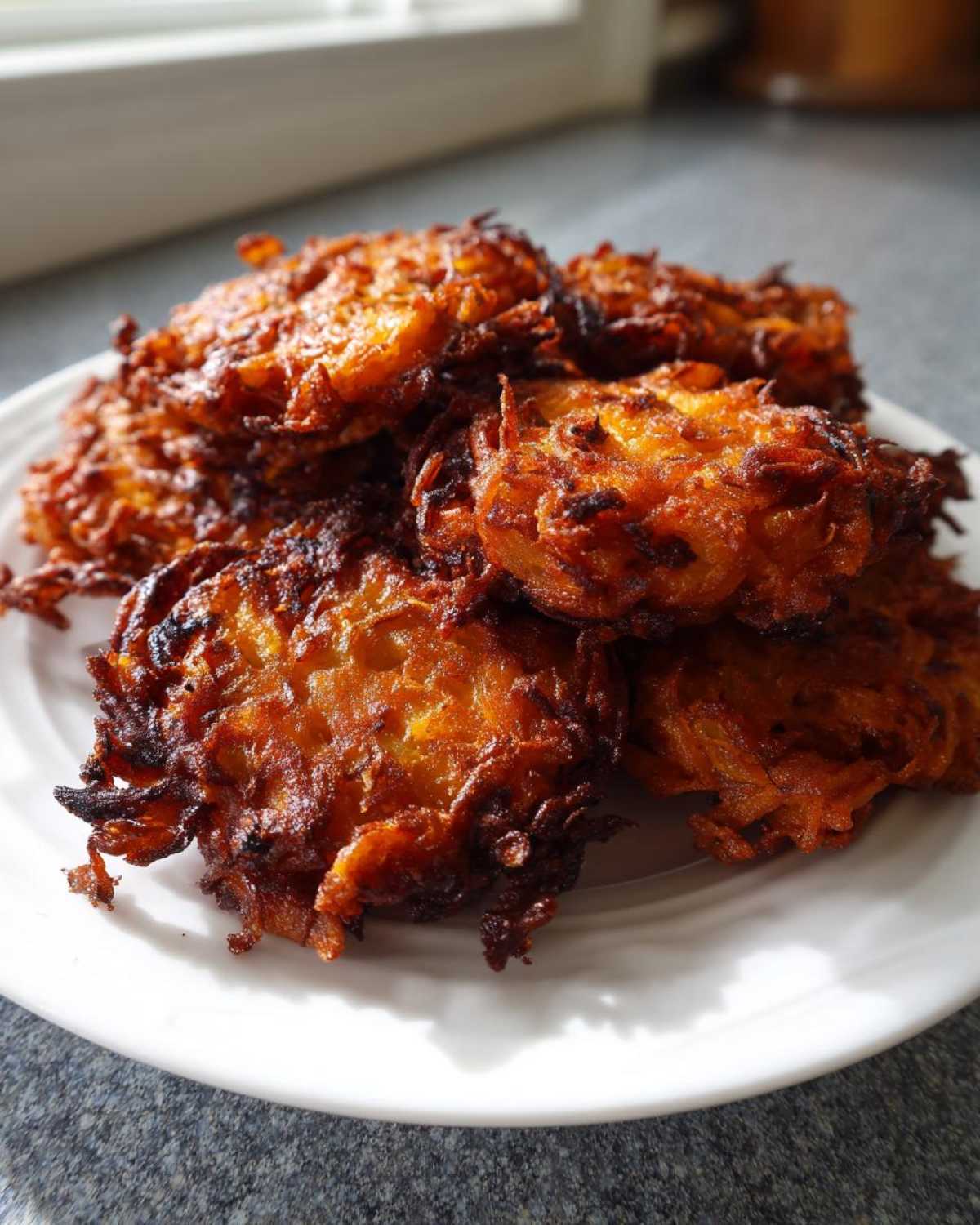 A close-up of several golden-brown, crispy Amish Onion Fritters piled high on a white plate.