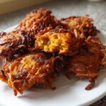 A close-up of several crispy, golden-brown Amish Onion Fritters piled on a white plate.
