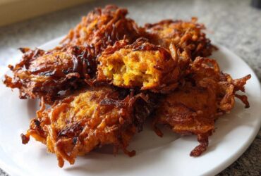 A close-up of several crispy, golden-brown Amish Onion Fritters piled on a white plate.