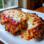 Close-up of a crispy chicken parmesan recipe cut open, showing melted mozzarella cheese stretching.