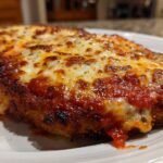 A close-up of a crispy, breaded chicken parmesan recipe topped with rich marinara sauce and bubbly, melted mozzarella cheese.