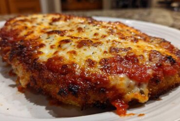 A close-up of a crispy, breaded chicken parmesan recipe topped with rich marinara sauce and bubbly, melted mozzarella cheese.