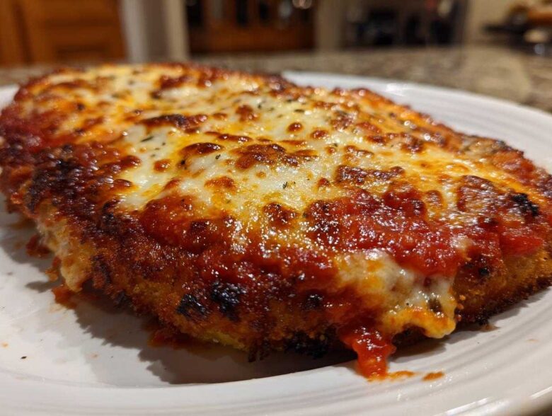 A close-up of a crispy, breaded chicken parmesan recipe topped with rich marinara sauce and bubbly, melted mozzarella cheese.
