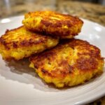 Close-up of three golden brown, crispy fried cornbread patties stacked on a white plate.