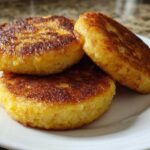 Three golden-brown, round patties of crispy fried cornbread stacked slightly on a white plate.
