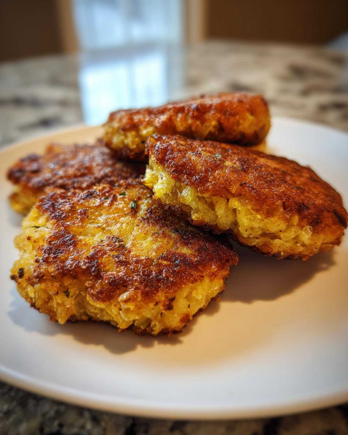 Close-up of four golden brown, crispy fried cornbread patties stacked on a white plate.