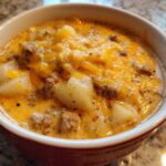 Close-up of a hearty bowl of crockpot cheeseburger soup, featuring chunks of potato, ground beef, and melted cheddar cheese.