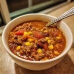 Close-up of a steaming white bowl filled with rich crockpot cowboy soup featuring ground beef, corn, tomatoes, and kidney beans.