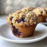 A close-up of a golden brown blueberry muffin topped with a thick layer of sweet streusel crumb topping.
