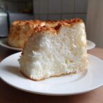 Close-up of a thick slice of airy, white angel food cake showing its spongy texture and light brown crust.