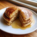 A stack of thick, fluffy discard pancakes drizzled generously with maple syrup, with a piece cut out.