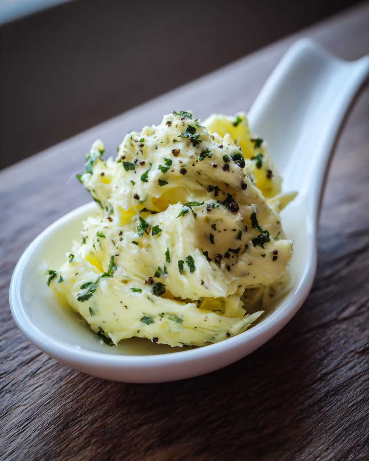 A dollop of creamy garlic butter mixed with chopped parsley and black pepper served in a white spoon.