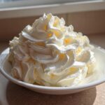 A generous mound of perfectly piped vanilla buttercream frosting in a small white bowl, highlighted by sunlight.