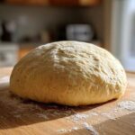 A perfectly rounded ball of fresh pizza dough resting on a floured wooden cutting board.