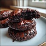 Close-up of three stacked, fudgy brownie cookies showing shiny, cracked tops and a soft interior.