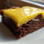 Close-up of a fudgy Lemon Brownies square topped with a thick, glossy layer of bright yellow lemon frosting.