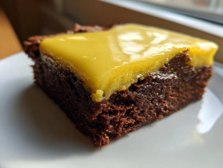 Close-up of a fudgy Lemon Brownies square topped with a thick, glossy layer of bright yellow lemon frosting.