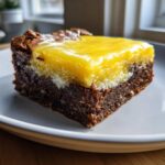 A close-up of a fudgy Lemon Brownies square topped with a thick layer of bright yellow lemon curd.