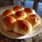 A cluster of six golden brown, shiny sourdough discard rolls arranged on a white plate.