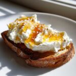 A close-up of gourmet ricotta toast topped with fluffy ricotta cheese, golden honey, and flaky salt.