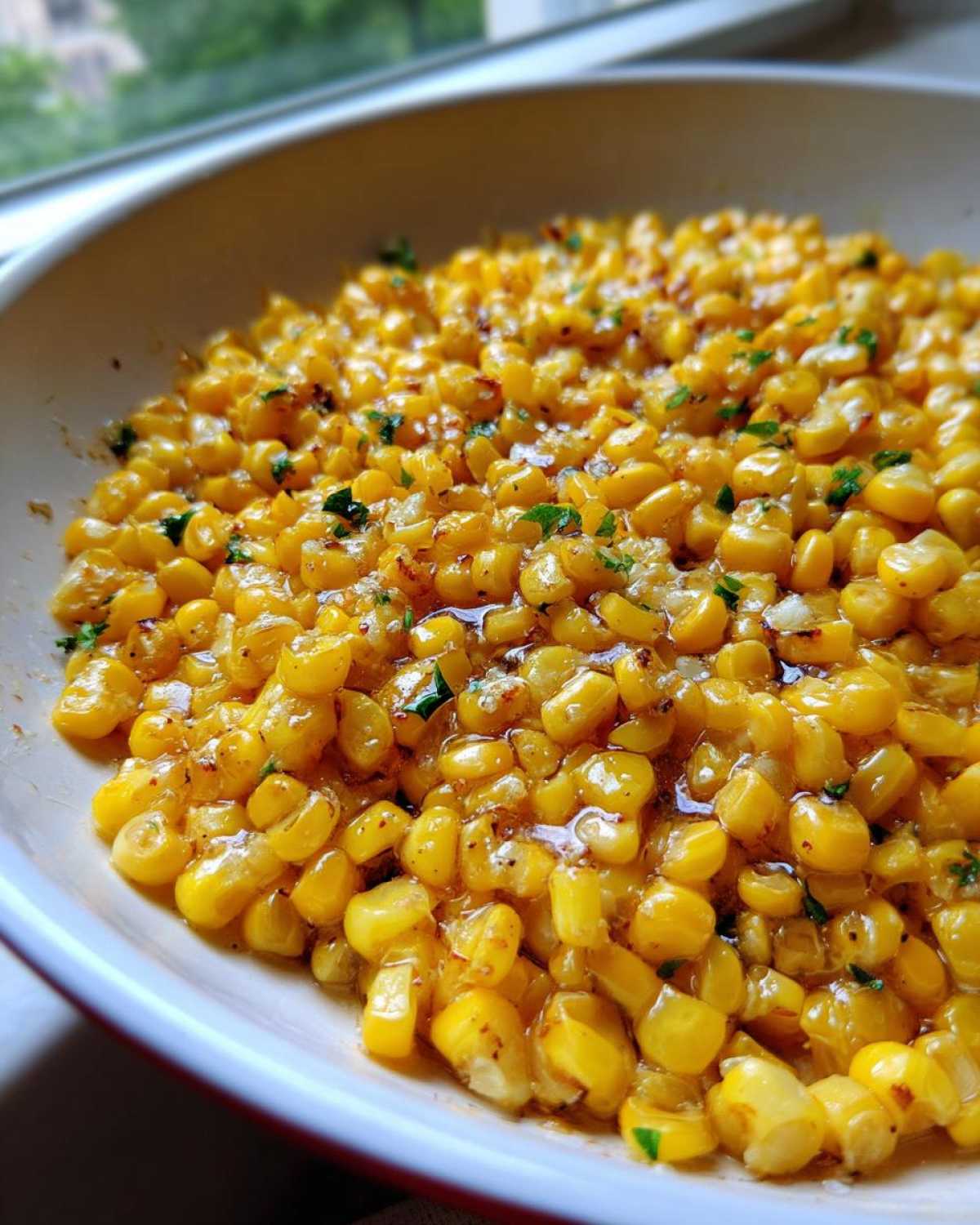 Close-up of glossy, bright yellow honey butter corn kernels garnished with green herbs in a white bowl.
