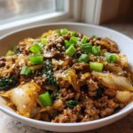 A close-up of a white bowl filled with keto egg roll in a bowl, topped with green onions and sesame seeds.