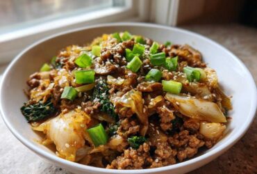 A close-up of a white bowl filled with keto egg roll in a bowl, topped with green onions and sesame seeds.