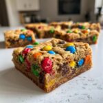 A close-up, delicious shot of a single square of christmas cookie bars studded with colorful M&Ms and chocolate chips.