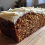 Close-up of a moist slice of brown applesauce cake topped with thick, creamy frosting.