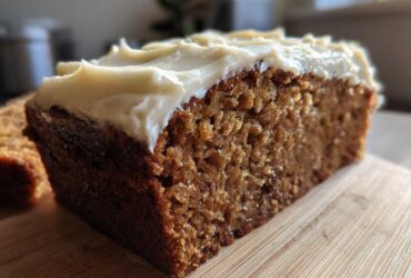 Close-up of a moist slice of brown applesauce cake topped with thick, creamy frosting.