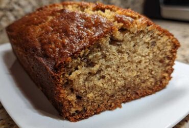 Close-up of a slice of moist banana bread showing its golden-brown, slightly glossy crust and tender crumb.