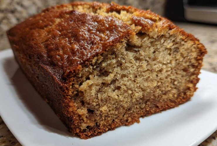 Close-up of a slice of moist banana bread showing its golden-brown, slightly glossy crust and tender crumb.