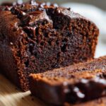 Close-up of a moist chocolate banana bread loaf, topped with melted chocolate chips, with one slice cut.