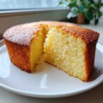 Close-up of a moist, golden-brown slice cut from a simple condensed milk cake on a white plate.