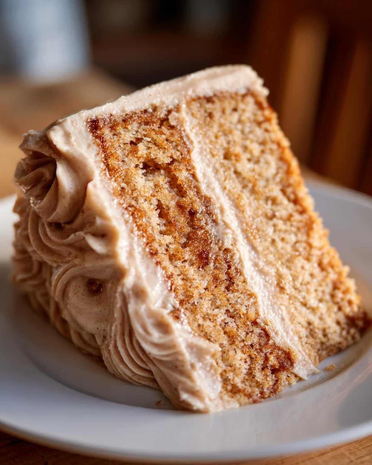 Close-up of a moist slice of spice cake layered with light brown frosting, served on a white plate.
