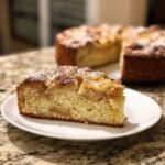 A close-up slice of moist Swedish apple cake dusted with powdered sugar on a white plate.