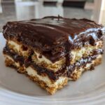 A close-up of a layered slice of no-bake chocolate eclair cake with creamy filling and glossy chocolate topping.