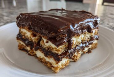 A close-up of a layered slice of no-bake chocolate eclair cake with creamy filling and glossy chocolate topping.