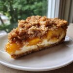 A perfect slice of peach cobbler cheesecake with a thick crumble topping and creamy filling.